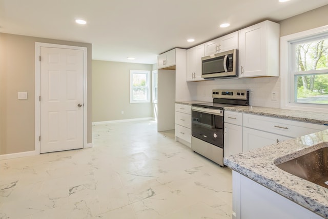 kitchen with appliances with stainless steel finishes, light stone counters, white cabinetry, baseboards, and recessed lighting