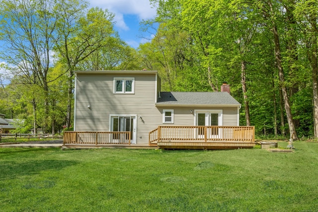 back of property featuring a chimney, a deck, and a lawn