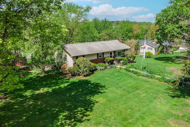 ranch-style house with brick siding, a front lawn, a chimney, and a forest view