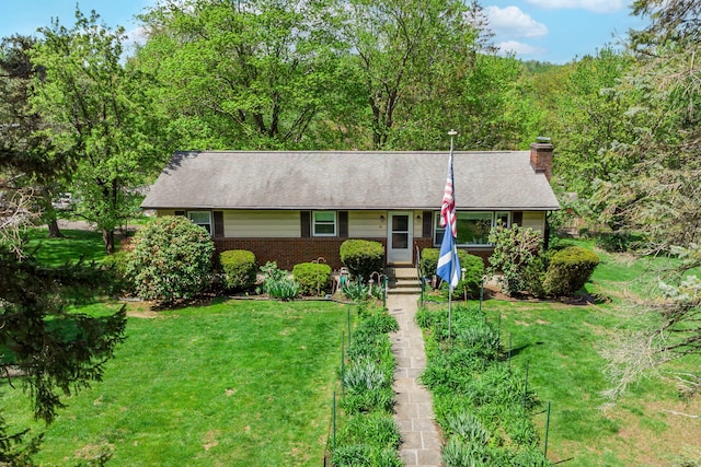single story home featuring a chimney, a front yard, brick siding, and a view of trees