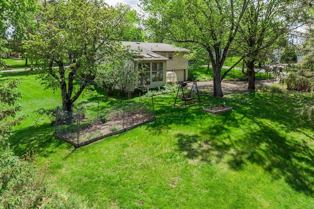 view of grassy yard featuring a garden, an attached garage, and a sunroom