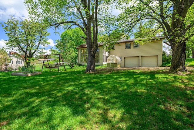 view of grassy yard with a vegetable garden, an attached garage, and a greenhouse