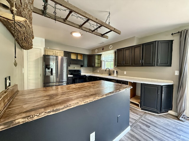 kitchen featuring stainless steel fridge with ice dispenser, black / electric stove, butcher block counters, light wood-style flooring, and a sink