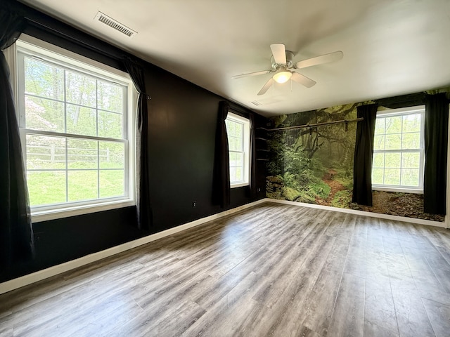spare room featuring healthy amount of natural light, wood finished floors, a ceiling fan, and baseboards