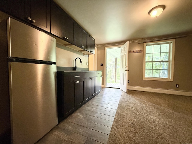 kitchen featuring freestanding refrigerator, baseboard heating, a sink, baseboards, and dark cabinets