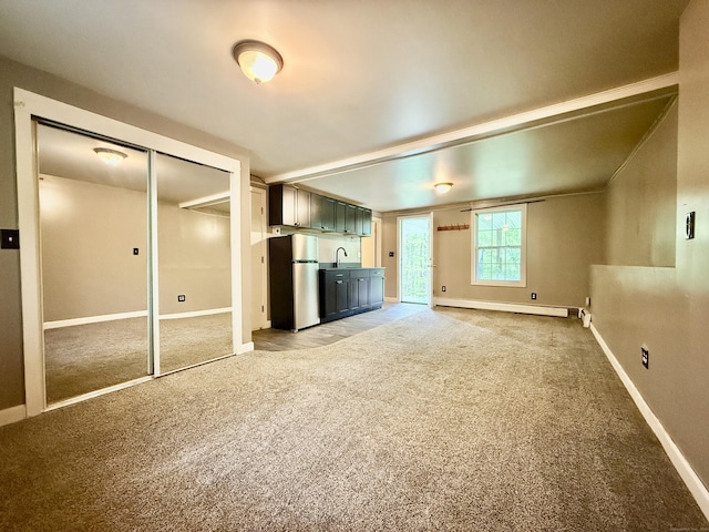 unfurnished living room featuring light carpet, a sink, and baseboards