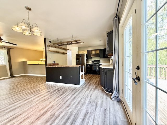 kitchen featuring stainless steel fridge, black electric range, light countertops, light wood-style flooring, and a sink