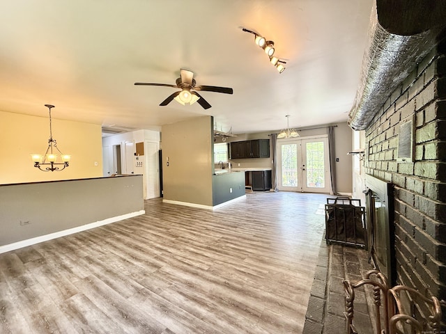 unfurnished living room with a brick fireplace, wood finished floors, a chandelier, a ceiling fan, and baseboards