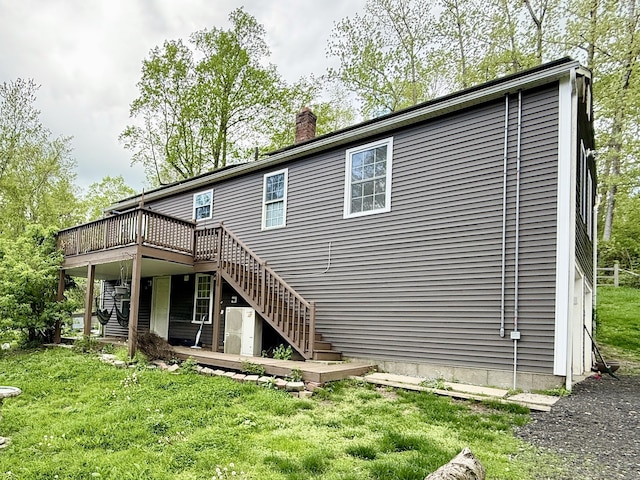 rear view of property with stairway, a wooden deck, a chimney, and a lawn
