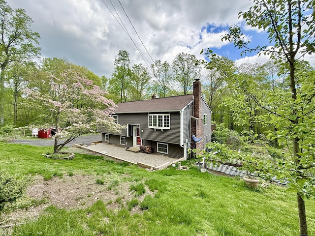 rear view of house with a garden, a chimney, a lawn, and a patio area