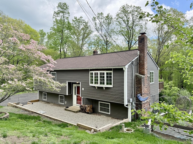back of property featuring a chimney, a patio, and a shingled roof