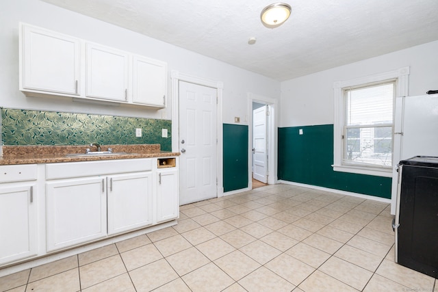 kitchen featuring a sink, white cabinets, freestanding refrigerator, range with electric stovetop, and baseboards