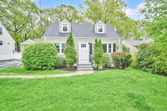 cape cod-style house featuring a shingled roof and a front yard