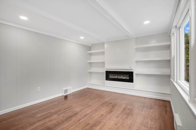 unfurnished living room featuring wood finished floors, a glass covered fireplace, beamed ceiling, built in shelves, and baseboards