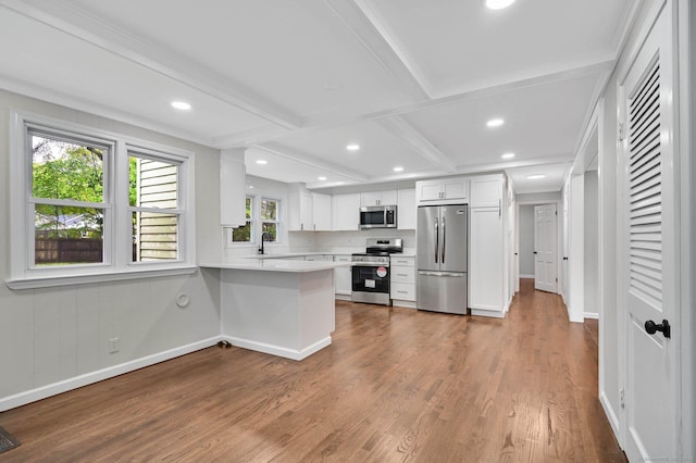 kitchen featuring appliances with stainless steel finishes, wood finished floors, coffered ceiling, light countertops, and white cabinetry