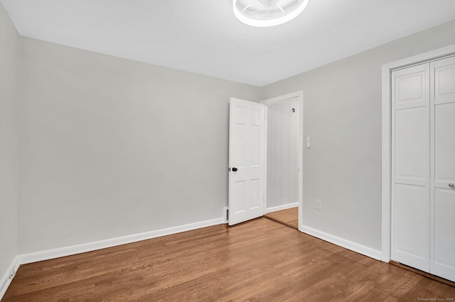 unfurnished bedroom featuring wood finished floors, baseboards, and a closet