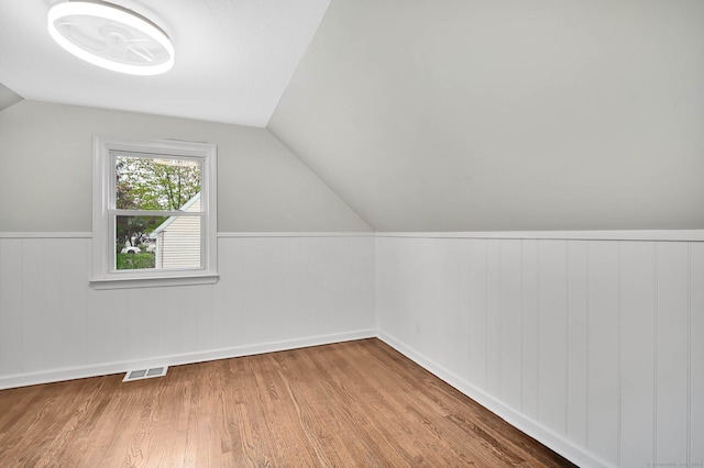 additional living space featuring wood finished floors, vaulted ceiling, a wainscoted wall, and baseboards
