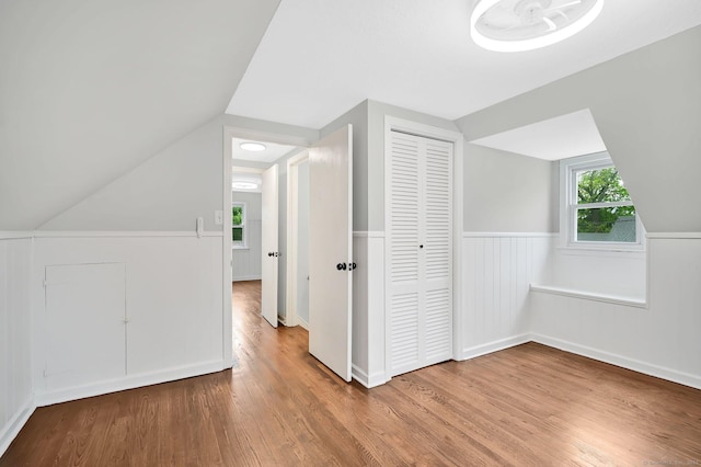 bonus room with wood finished floors, vaulted ceiling, and wainscoting