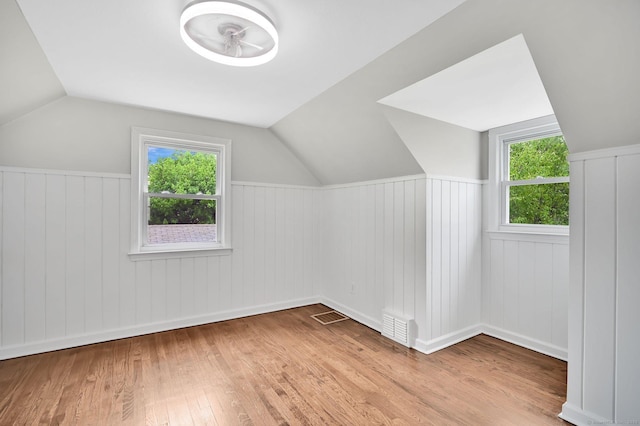 bonus room with wood finished floors, vaulted ceiling, wainscoting, and healthy amount of natural light