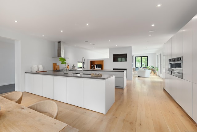 kitchen featuring wall chimney range hood, modern cabinets, dark countertops, open floor plan, and white cabinetry