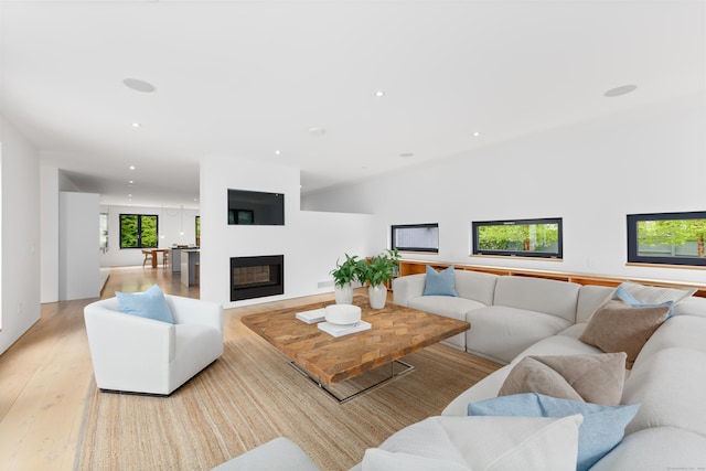 living room featuring light wood-style flooring, recessed lighting, and a glass covered fireplace