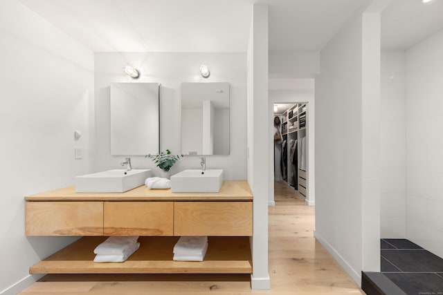bathroom with wood finished floors, double vanity, a walk in closet, and baseboards