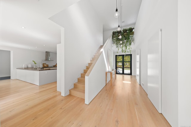 foyer entrance featuring stairs, light wood-type flooring, and a high ceiling