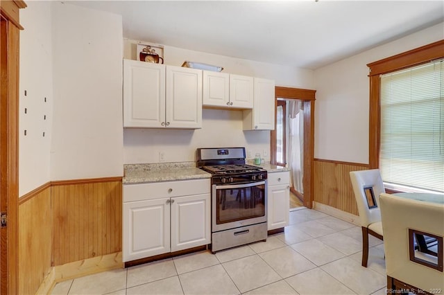 19 5th St, Ansonia, CT 06401 - kitchen featuring gas stove, wainscoting, wooden walls, white cabinetry, and light tile patterned flooring