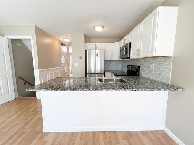 279 New Haven Ave Apt H, Milford, CT 06460 - kitchen featuring appliances with stainless steel finishes, a peninsula, dark stone countertops, light wood-style floors, and a sink