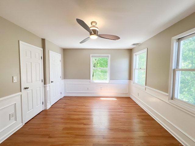 279 New Haven Ave Apt H, Milford, CT 06460 - empty room featuring healthy amount of natural light, wainscoting, light wood-type flooring, ceiling fan, and a decorative wall