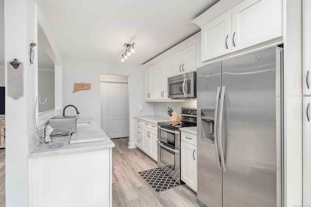 kitchen with stainless steel appliances, a sink, light wood-type flooring, white cabinets, and decorative backsplash