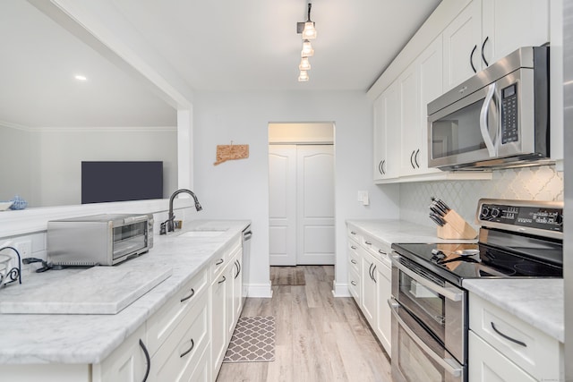 kitchen featuring stainless steel appliances, a sink, backsplash, white cabinets, and light wood finished floors