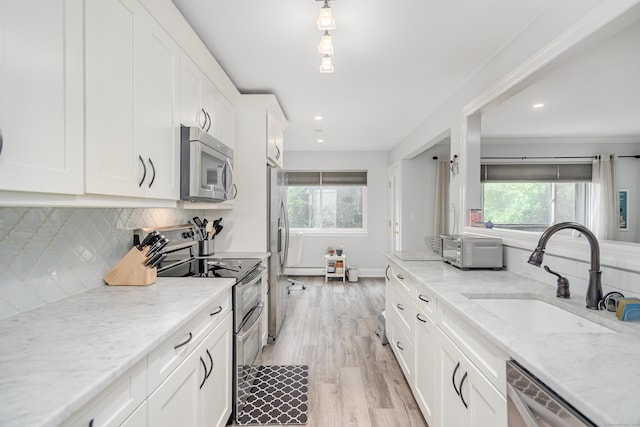 kitchen with stainless steel appliances, a sink, white cabinets, light wood-style flooring, and decorative backsplash