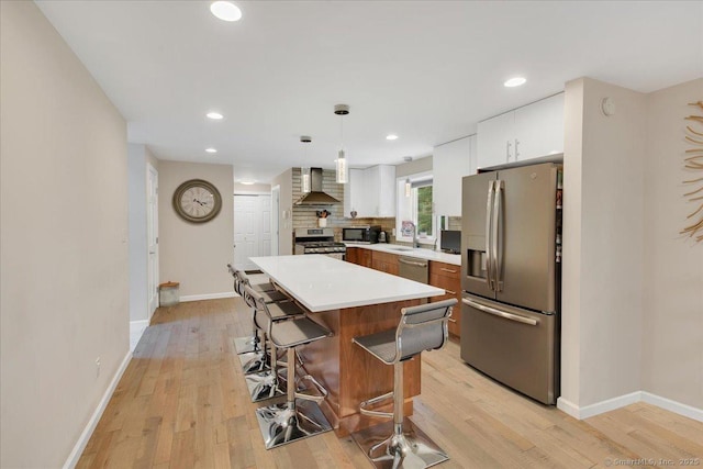 kitchen featuring stainless steel appliances, wall chimney range hood, baseboards, a breakfast bar area, and light wood finished floors