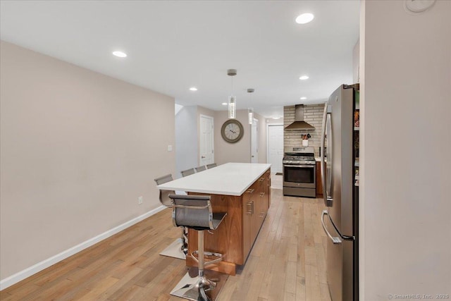 kitchen featuring stainless steel appliances, wall chimney exhaust hood, light wood-style floors, light countertops, and a kitchen island
