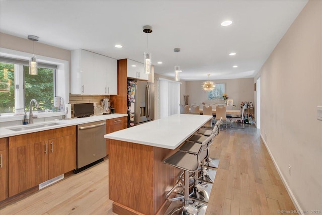 kitchen featuring stainless steel appliances, a sink, a kitchen breakfast bar, light wood-style flooring, and white cabinetry