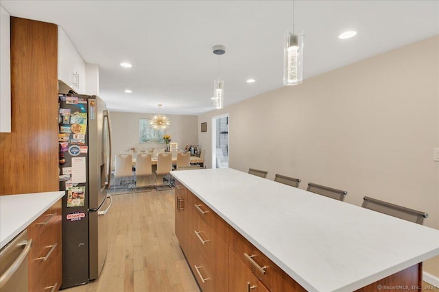 kitchen with appliances with stainless steel finishes, a kitchen island, light countertops, light wood finished floors, and brown cabinetry