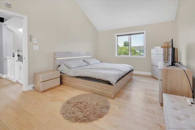 bedroom with light wood finished floors, lofted ceiling, and baseboards
