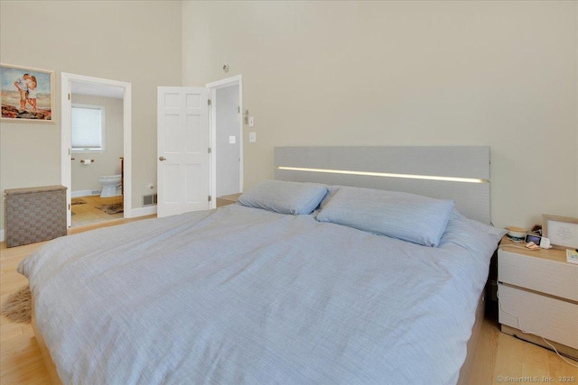 bedroom featuring light wood-style flooring, a towering ceiling, ensuite bath, and baseboards