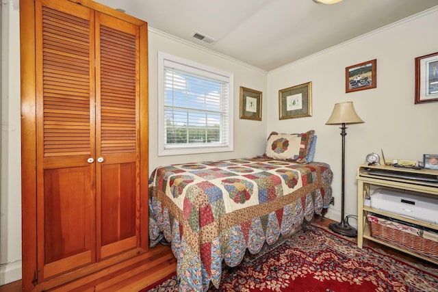 bedroom with wood finished floors, crown molding, and a closet