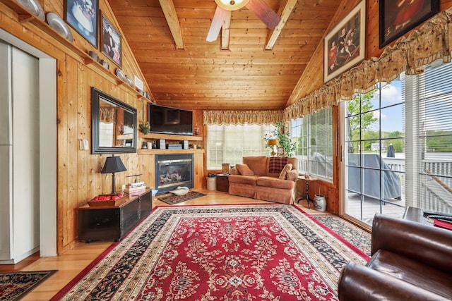 living room featuring wood ceiling, wood finished floors, wood walls, a glass covered fireplace, and a ceiling fan