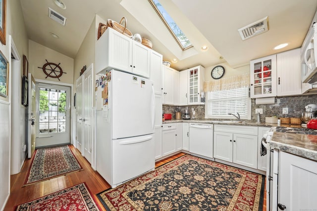 kitchen featuring white appliances, vaulted ceiling, a skylight, tasteful backsplash, and light wood-style flooring