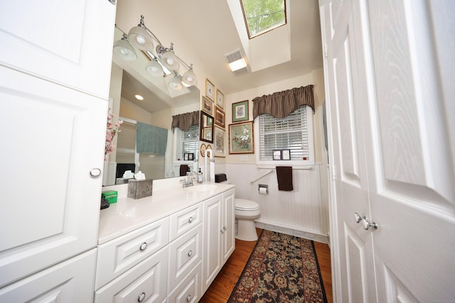 bathroom with toilet, vanity, wood finished floors, a wainscoted wall, and a shower with shower door