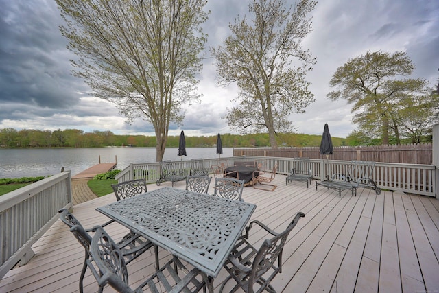 deck with outdoor dining space, a water view, fence, and an outdoor fire pit