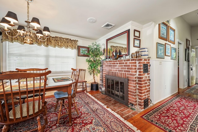 dining room with a chandelier, a brick fireplace, wood finished floors, and a wainscoted wall