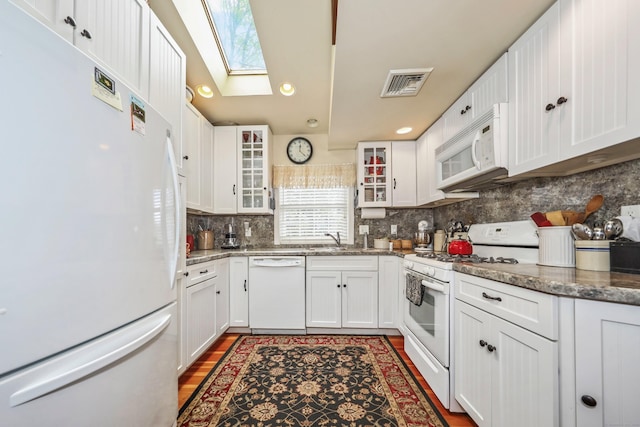 kitchen featuring white appliances, a skylight, white cabinetry, decorative backsplash, and glass insert cabinets