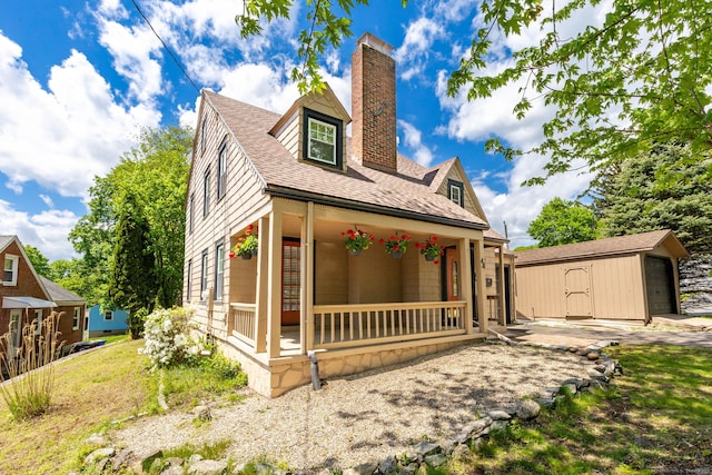 view of front of house with covered porch, an outdoor structure, a chimney, and roof with shingles