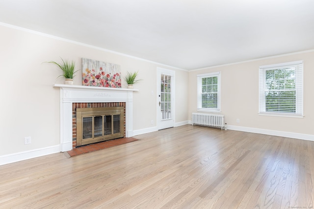 unfurnished living room with radiator, ornamental molding, a fireplace, wood finished floors, and baseboards