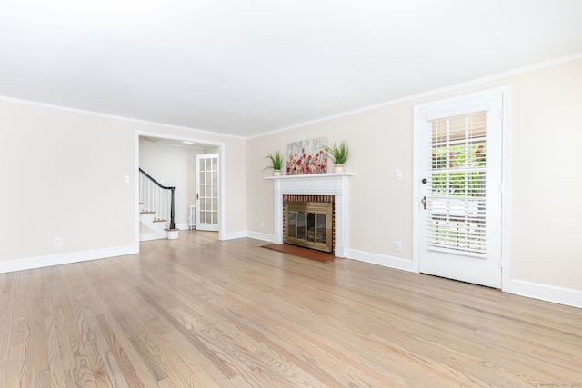unfurnished living room with a fireplace, stairs, light wood-style floors, baseboards, and crown molding