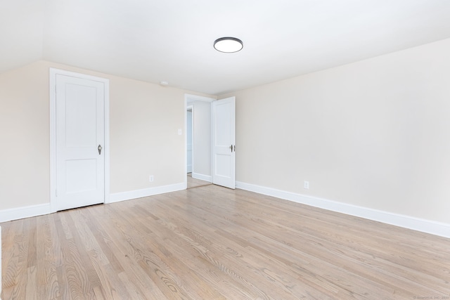 unfurnished room with light wood finished floors, baseboards, and lofted ceiling